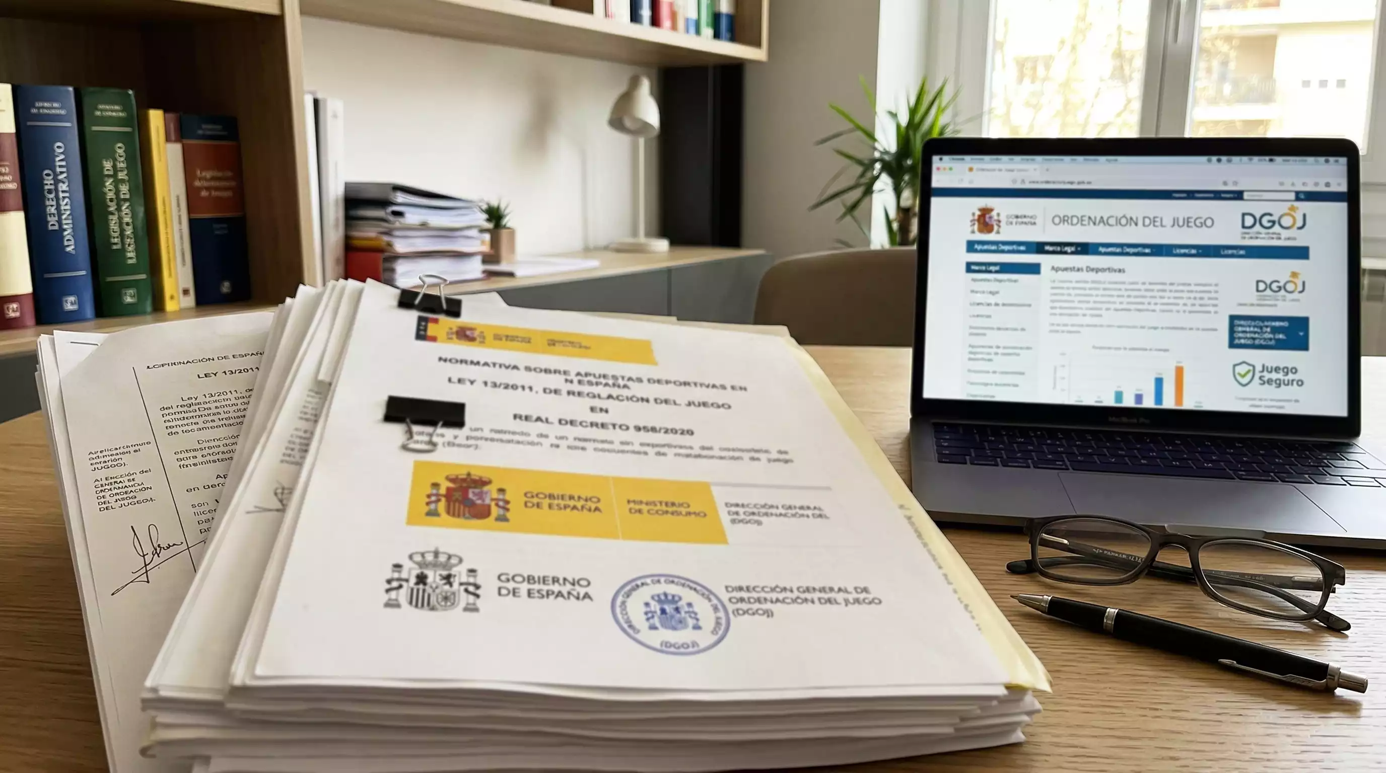 Documento legal y sello oficial junto a un portátil con la web de la DGOJ abierta